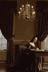a woman in a long dress sits at a desk writing in a book