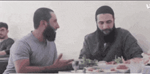 two men are sitting at a table talking to each other .