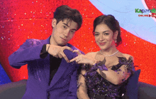 a man in a purple suit and a woman in a purple dress are making a heart shape with their hands ..