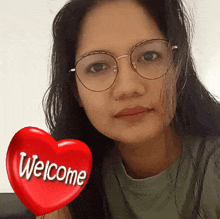 a woman wearing glasses has a red heart with welcome written on it