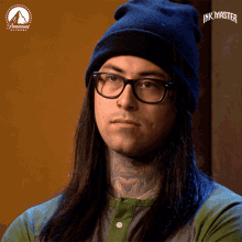a man with long hair wearing glasses and a beanie with the word ink master on the bottom
