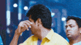 a man in a yellow shirt is covering his eyes with his hand
