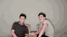 two young men are sitting next to each other on a bed and giving each other a thumbs up .