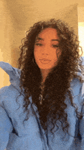 a woman with curly hair wearing a blue jacket and hoop earrings .