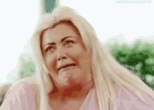 a woman with long blonde hair is making a funny face while wearing a pink shirt .
