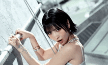 a woman with short black hair is wearing a white tank top and a silver chain around her neck