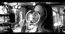 a black and white photo of a woman wearing hoop earrings and holding a glass of wine .