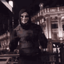 a person wearing a mask and a hood is standing in front of a building at night .