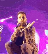 a man in a leopard print jacket is singing into a microphone on a stage with purple lights behind him .