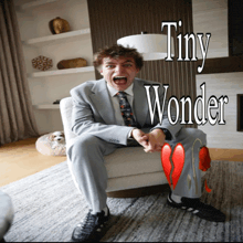 a man in a suit and tie is sitting in a chair with tiny wonder written on the bottom