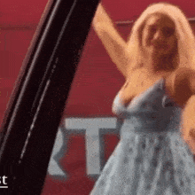 a woman in a blue dress is dancing in front of a red wall .