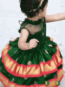 a little girl is wearing a green dress with red and gold trim .