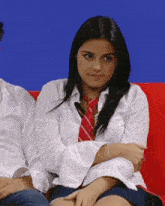 a woman wearing a white shirt and red tie sits on a red couch