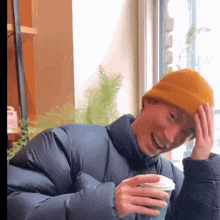a man wearing a yellow beanie is smiling while holding a cup of coffee