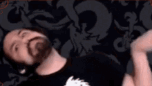 a man with a beard is laying on his stomach on a bed with his head down .