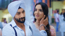 a man wearing a turban is touching the face of a woman .