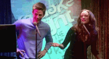 a man and a woman are singing into microphones in front of a sign that says ' the point ' on it