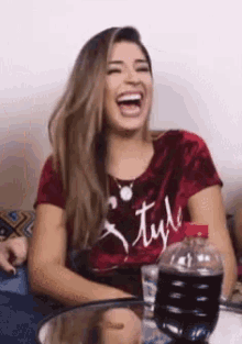a woman is laughing while sitting at a table with a bottle of coke in front of her .