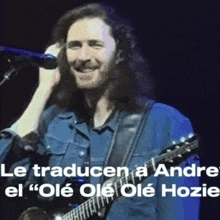 a man with long hair is singing into a microphone while playing a guitar .
