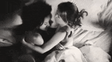 a black and white photo of two women hugging each other in bed .