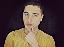 a man wearing a yellow shirt with the letter k on it holds his hand to his chin