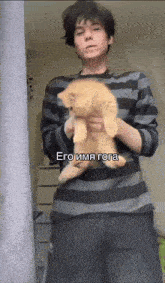 a man in a striped shirt is holding a small orange cat in his arms .