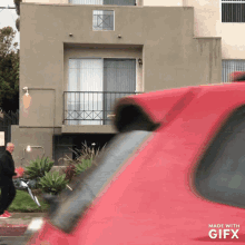 a red car is parked in front of a building with a sign that says made with gifx