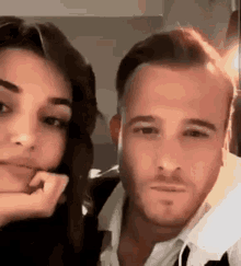 a man and a woman are posing for a picture together and the woman is covering her mouth with her hand .