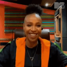 a woman with a shaved head is smiling while sitting in a chair in front of a colorful wall .