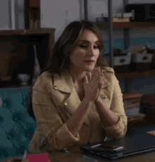 a woman wearing a yellow jacket sits at a desk with her hands folded