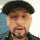 a man with a beard is wearing a black hat and making a funny face