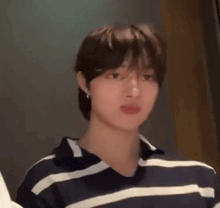 a young man wearing a striped shirt and earrings is standing in a room .
