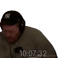 a man wearing headphones and a ny hat is sitting in front of a screen that says 10 : 07 : 32