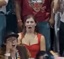 a woman in a red dress is sitting in a crowd of people with her mouth open .