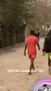 a man in a red shirt and shorts is walking down a dirt road