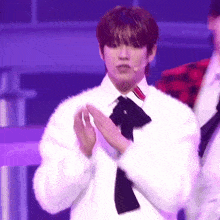 a young man in a white shirt and black tie is clapping his hands .