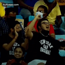 a man wearing a mask and a new york gap original t-shirt is sitting in a stadium .
