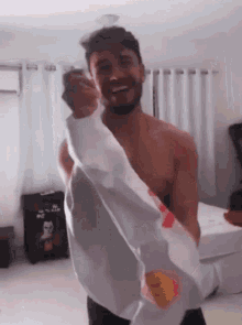 a shirtless man is holding a white shirt in a room