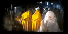 a group of people in yellow cloaks are walking in a dark room
