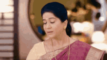 a woman wearing a pink saree and pearls is standing in a room .