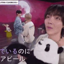 a woman is holding a stuffed panda bear in front of a group of people in a room .