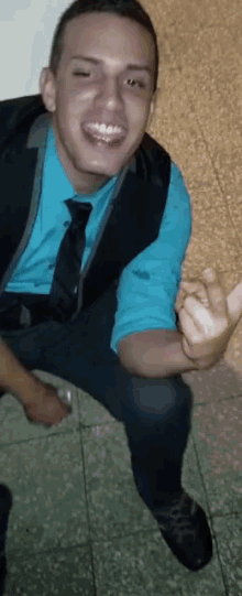 a man in a blue shirt and tie is smiling and giving the middle finger