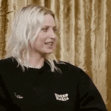 a woman with long blonde hair is wearing a black sweatshirt with the word basta on it .