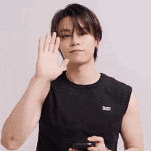 a young man in a black sleeveless shirt is holding a cell phone and waving .