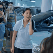 a woman in a blue shirt is standing in front of cars