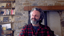 a man in a plaid shirt is sitting in front of a stone wall and a sign that says " keep it simple "