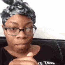 a woman wearing glasses and a headband is sitting on a couch and making a funny face .