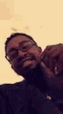 a man wearing glasses and a black turtleneck is smiling and taking a selfie .