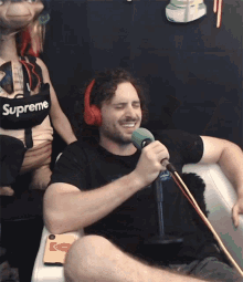a man wearing red headphones and a black supreme shirt is singing into a microphone