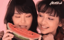 two women are eating a slice of watermelon together and smiling .